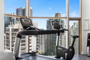 Ein Heimfitnessraum mit Laufband und Ergometer, große Fenster mit Blick auf die Stadt.