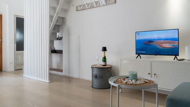 A modern living room with a flat-screen TV, a small round table with decorative items, a metal barrel, and a staircase. - Dream Loft Roma 100 - Goelba (Capoliveri)