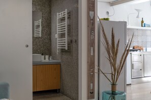 Ein modernes Badezimmer mit gefliestem Rückspritzschutz, einem hölzernen Waschtisch, einem weißen Handtuchhalter und einer dekorativen Vase mit Trockenpflanzen.