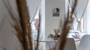 A dining area with a table and chairs, a wall clock, and a window with curtains. - Dream Loft Roma 100 - Goelba (Capoliveri)