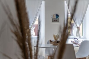 Ein Essbereich mit Tisch und Stühlen, einer Wanduhr und einem Fenster mit Vorhängen.