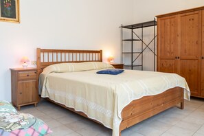 A bedroom with a wooden bed, two bedside tables with lamps, a wardrobe, and a metal shelving unit. - Le Cote di Seccheto - Goelba (Campo nell'Elba)