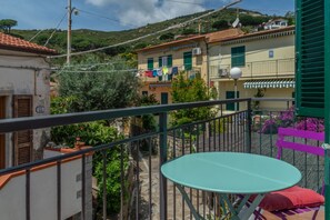 A balcony with a table and chairs, a view of neighboring buildings, and a green fence. - Le Cote di Seccheto - Goelba (Campo nell'Elba)