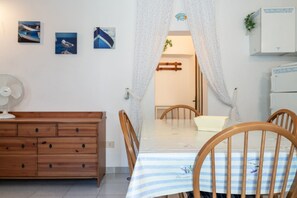 Una stanza con un comò in legno, un tavolo con tovaglia a righe, una ventola e tre quadri appesi al muro.