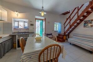 A dining area with a striped tablecloth, wooden chairs, a kitchen with a window, and a wooden staircase. - Le Cote di Seccheto - Goelba (Campo nell'Elba)
