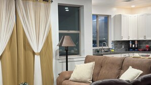 Ein Wohnzimmer mit einer Couch, einer Lampe, einem Fenster und einer Küchenzeile mit Schränken und einem Spülbecken.