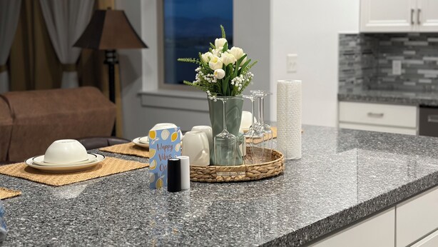Eine moderne Küche mit Granit-Arbeitsplatten, einem Blumenstrauß und einer Frühstücksecke mit Kaffeemaschine und einer Karte.