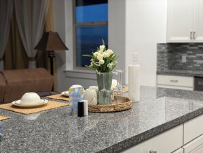 A modern kitchen with granite countertops, a vase of flowers, and a breakfast setting with a coffee maker and a card.