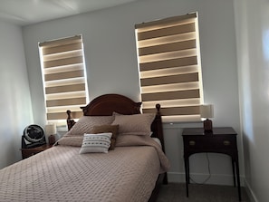 A bedroom with a bed, two bedside tables, a lamp, and a fan.