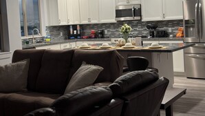 A modern kitchen with white cabinets, stainless steel appliances, and a dining area with a brown leather couch.