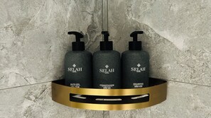 Drie flessen Selah Hotel toiletartikelen op een plank met gouden rand, voor een structuurwand.