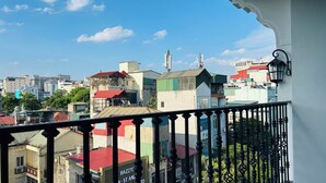Ein Balkon mit Blick auf eine Stadtlandschaft, darunter Gebäude in verschiedenen Baustilen und einem klaren Himmel.