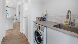 A modern kitchen with a built-in washer, a stainless steel sink, and a tiled backsplash. - Cosy Sun trap, Close to beach and the iconic yellow Dairy. (Waihi Beach)