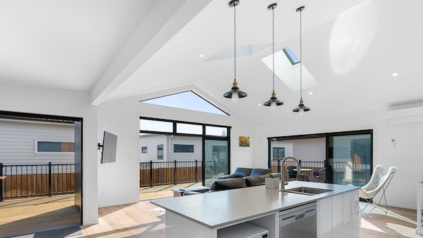 A modern kitchen with a central island, built-in appliances, and a large sliding glass door leading to a deck. - Cosy Sun trap, Close to beach and the iconic yellow Dairy. (Waihi Beach)