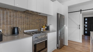 A modern kitchen with white cabinets, a stainless steel stove, and a refrigerator. - Cosy Sun trap, Close to beach and the iconic yellow Dairy. (Waihi Beach)