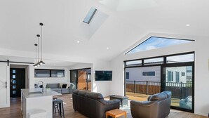 A spacious living area with a kitchen, seating, and a large sliding glass door to a deck. - Cosy Sun trap, Close to beach and the iconic yellow Dairy. (Waihi Beach)