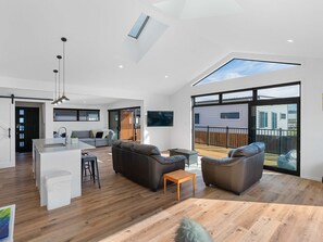 Ein geräumiger Wohnbereich mit einer Küche, Sitzgelegenheiten und einer großen Schiebeglasdoor zum Deck.