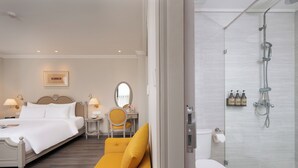 A hotel room with a bed, a sofa, a bathroom with a shower, and a small table with a chair. - Elegant European Luxury in the Heart of Sapa (Sa Pa)