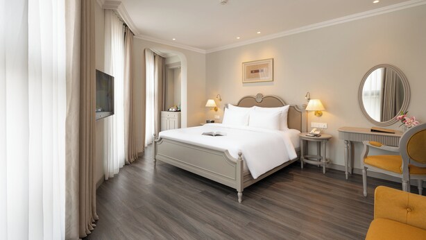 A hotel room with a bed, bedside tables, a chair, a mirror, and a television. - Elegant European Luxury in the Heart of Sapa (Sa Pa)