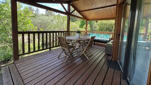 A wooden deck with a table and chairs, a bench, and a view of greenery.