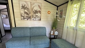 A room with a grey sofa, a small side table with a vase and a candle, and a wall with a botanical print.