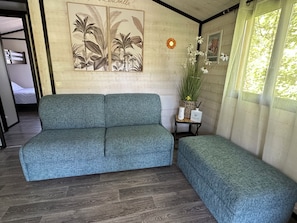 A room with a grey sofa, a small side table with a vase and a candle, and a wall with a botanical print.