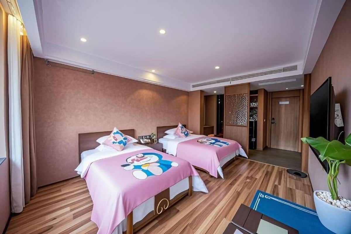 Quarto de hotel com duas camas, televisão, uma planta e piso de madeira.