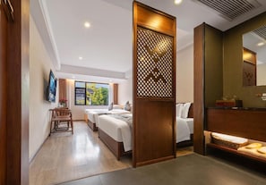 Ein Hotelzimmer mit Holzabtrennung, einem Bett, einem Schreibtisch, einem Stuhl und einem Fenster mit Blick auf Grünflächen.
