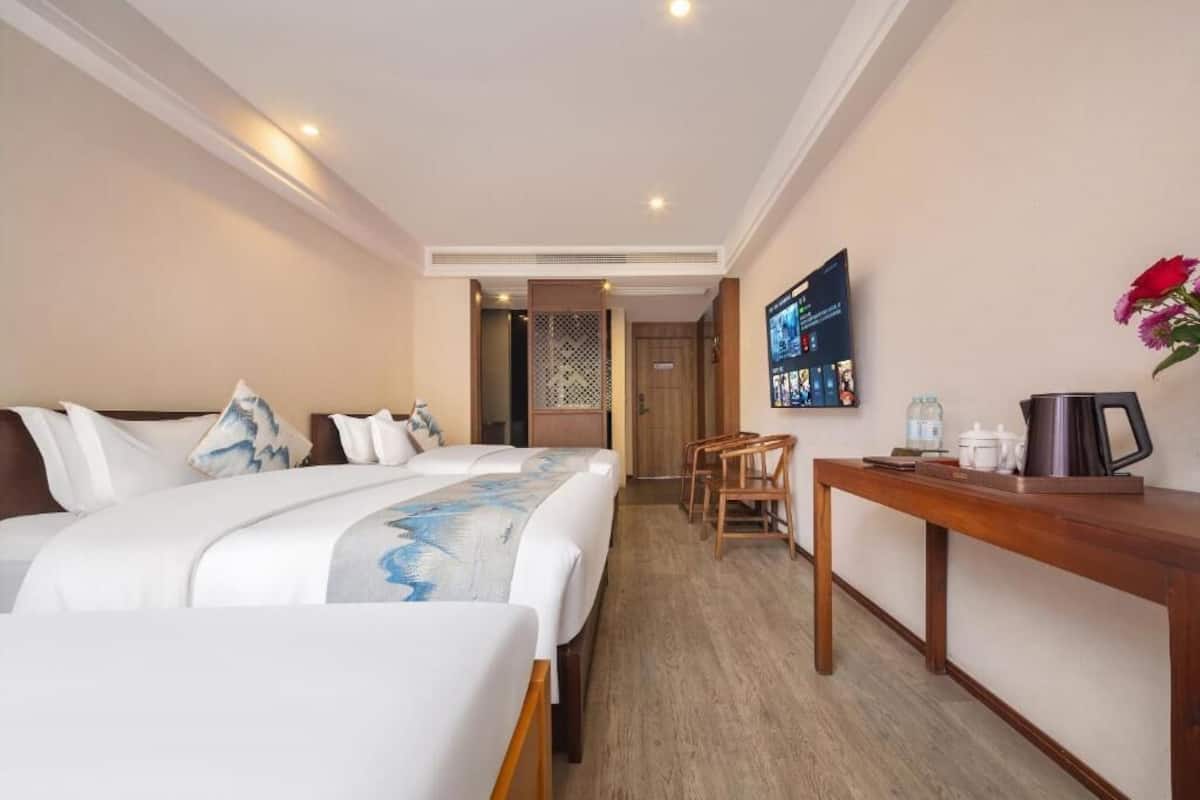 Quarto de hotel com cama, escrivaninha, cadeira e uma pequena mesa com chaleira e chávenas.