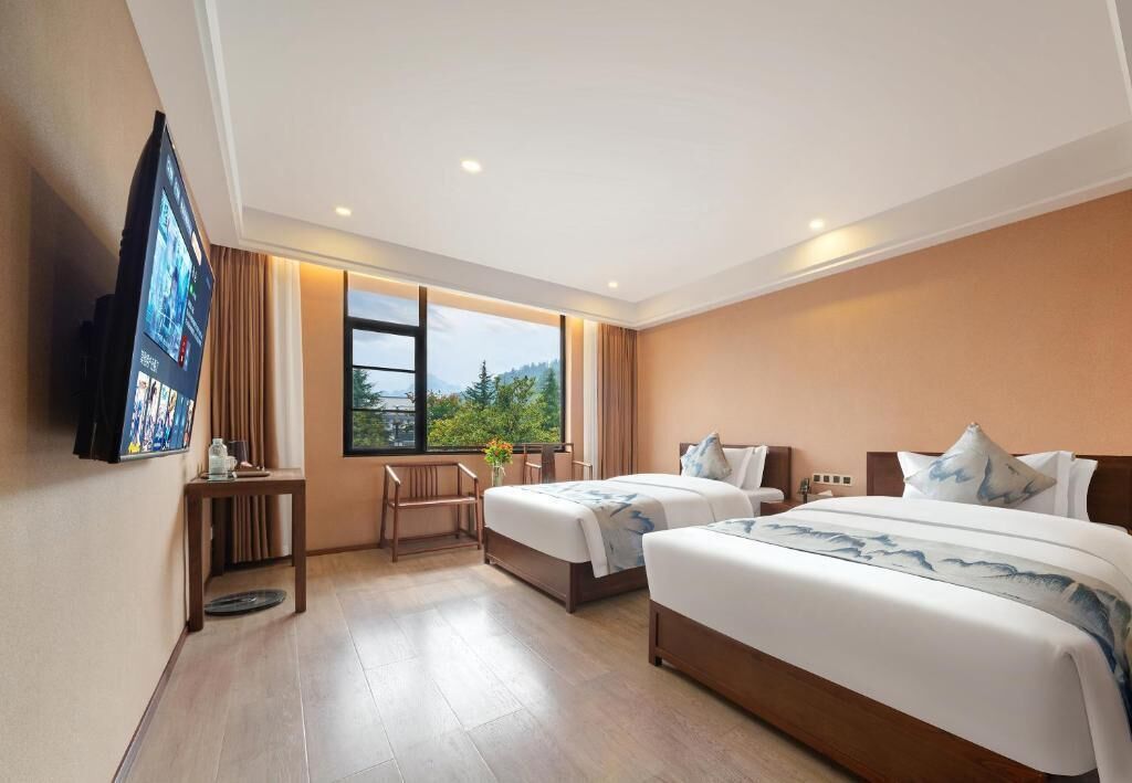 Habitación de hotel con dos camas, un televisor, una ventana con vistas y una pequeña mesa con una silla.