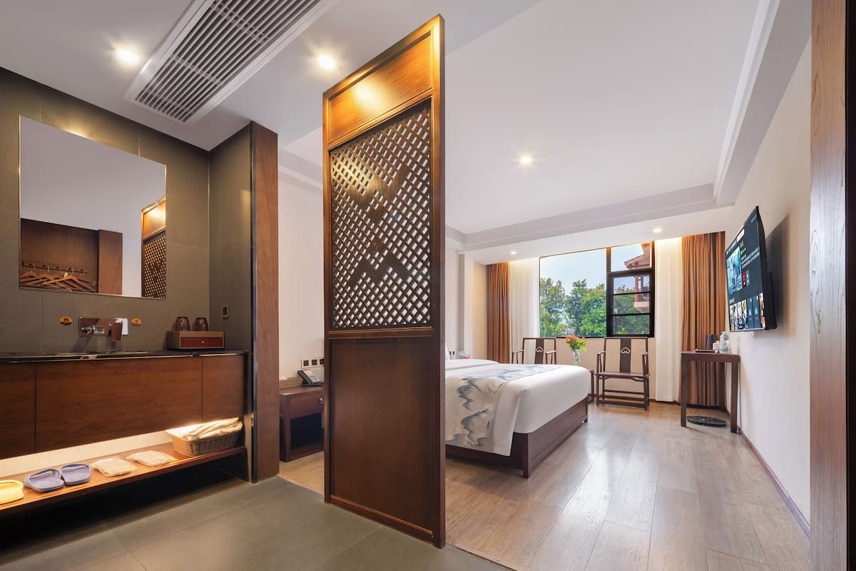 Quarto de hotel com cama, escrivaninha, televisão, banheiro com espelho e janela com vista.