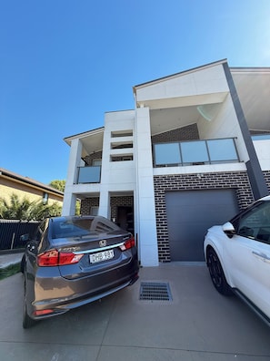 A modern two-story house with a garage, a driveway, and two parked cars.