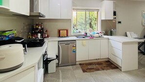 A modern kitchen with white cabinets, a built-in oven, a dishwasher, and a window providing natural light.