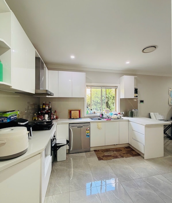 A modern kitchen with white cabinets, a built-in oven, a dishwasher, and a window providing natural light.
