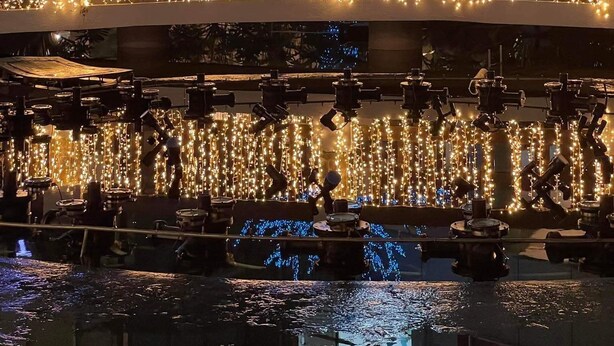 Een gebouw met een boom versierd met blauwe lichtjes, een waterpartij en lichtslingers.