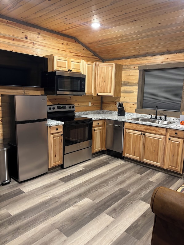 A modern kitchen with wooden cabinets, stainless steel appliances, and a herringbone-patterned floor.