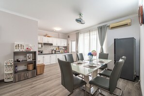 Eine moderne Küche mit weißen Schränken, einem Essbereich mit Glastisch und Stühlen sowie einem Kühlschrank.
