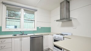 Eine Küche mit weißen Schränken, einem Geschirrspüler, einem Herd und einem Fenster mit Jalousien.