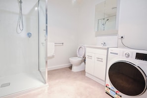 Une salle de bain avec une douche à parois de verre, des toilettes, un lave-linge et un miroir au-dessus du lavabo.