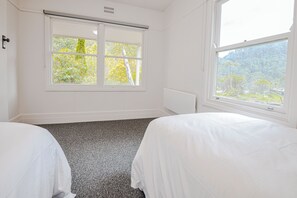 A hotel room with two beds, a radiator, a window with blinds, and a view of trees. - StayAU Alpine Retreat Family FALLS CREEK (Bogong)