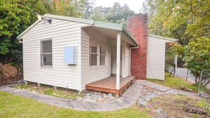 Ein kleines, eingeschossiges Haus mit Veranda, Backsteinsschornstein und einem kleinen angebauten Schuppen.