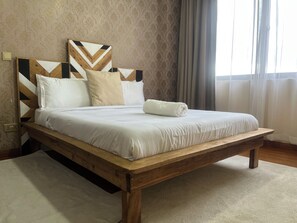 Ein Bett mit Holzrahmen und einem Kopfteil mit geometrischen Mustern, eine weiße Bettdecke und ein aufgerolltes weißes Handtuch.