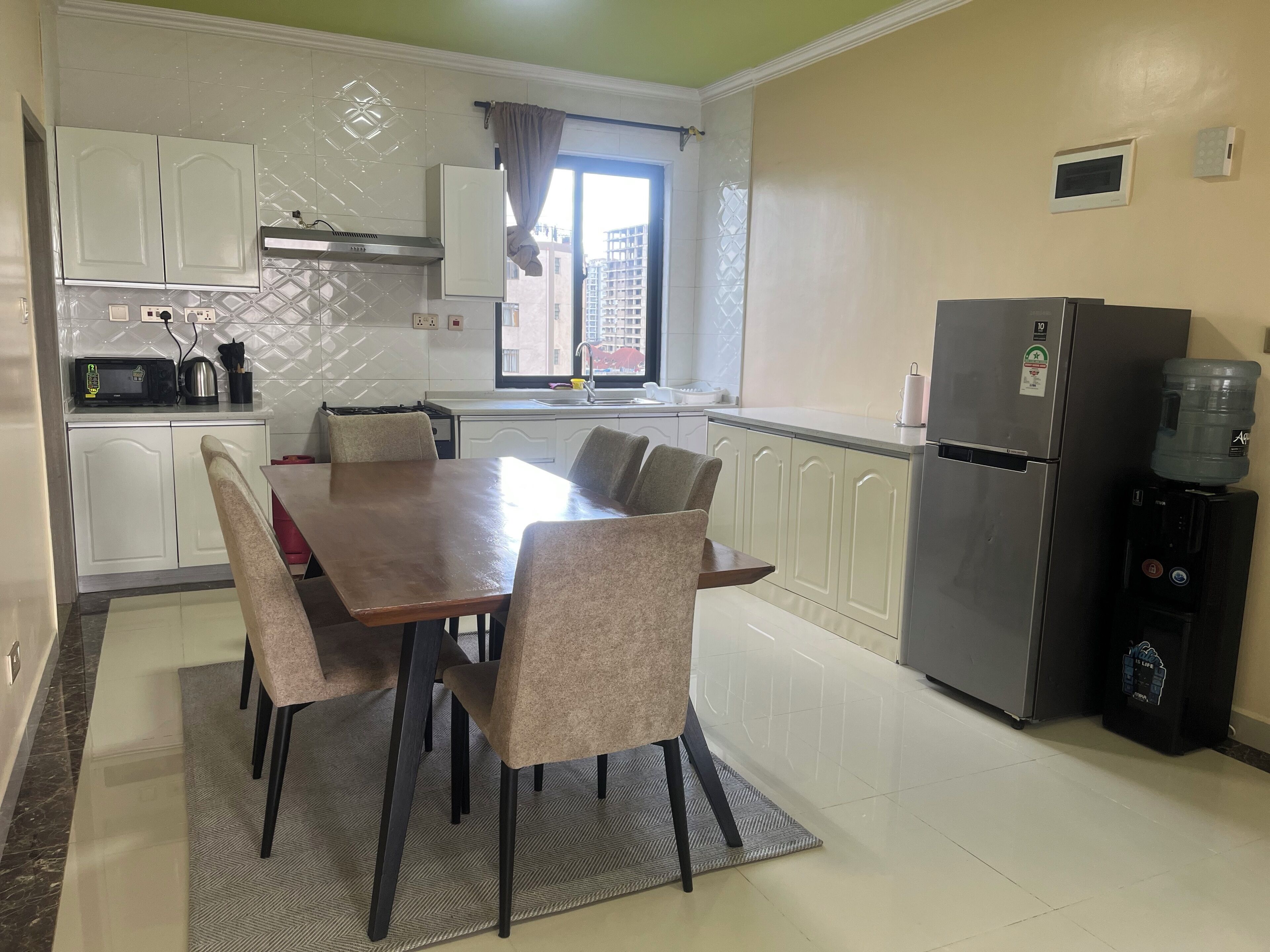 A modern kitchen with a dining table, chairs, a refrigerator, and a water dispenser.
