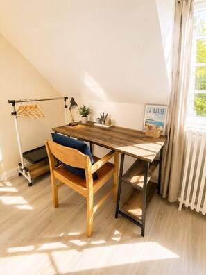 A room with a wooden desk, a chair, a radiator, a window with curtains, a coat rack, and a framed picture. - Escale Laponneraye – Proche gare & centre (Tours)