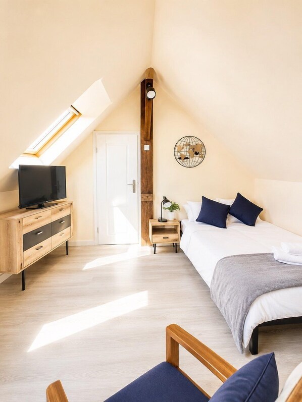 Ein Schlafzimmer mit schräg steilender Decke, einem Fernseher auf einer Holzkommode, einem Nachttisch mit Lampe, einem Bett mit Kissen und einer an der Wand befestigten Globen-Dekoration.