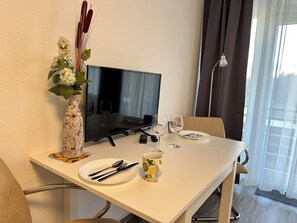 Ein Hotelzimmer mit Esstisch für zwei Personen, einem Flachbildfernseher, einer Vase mit Blumen und Blick ins Freie.