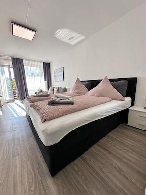 Ein modernes Schlafzimmer mit schwarzem Bettgestell, weißer Bettwäsche und einem großen Fenster mit Vorhängen.