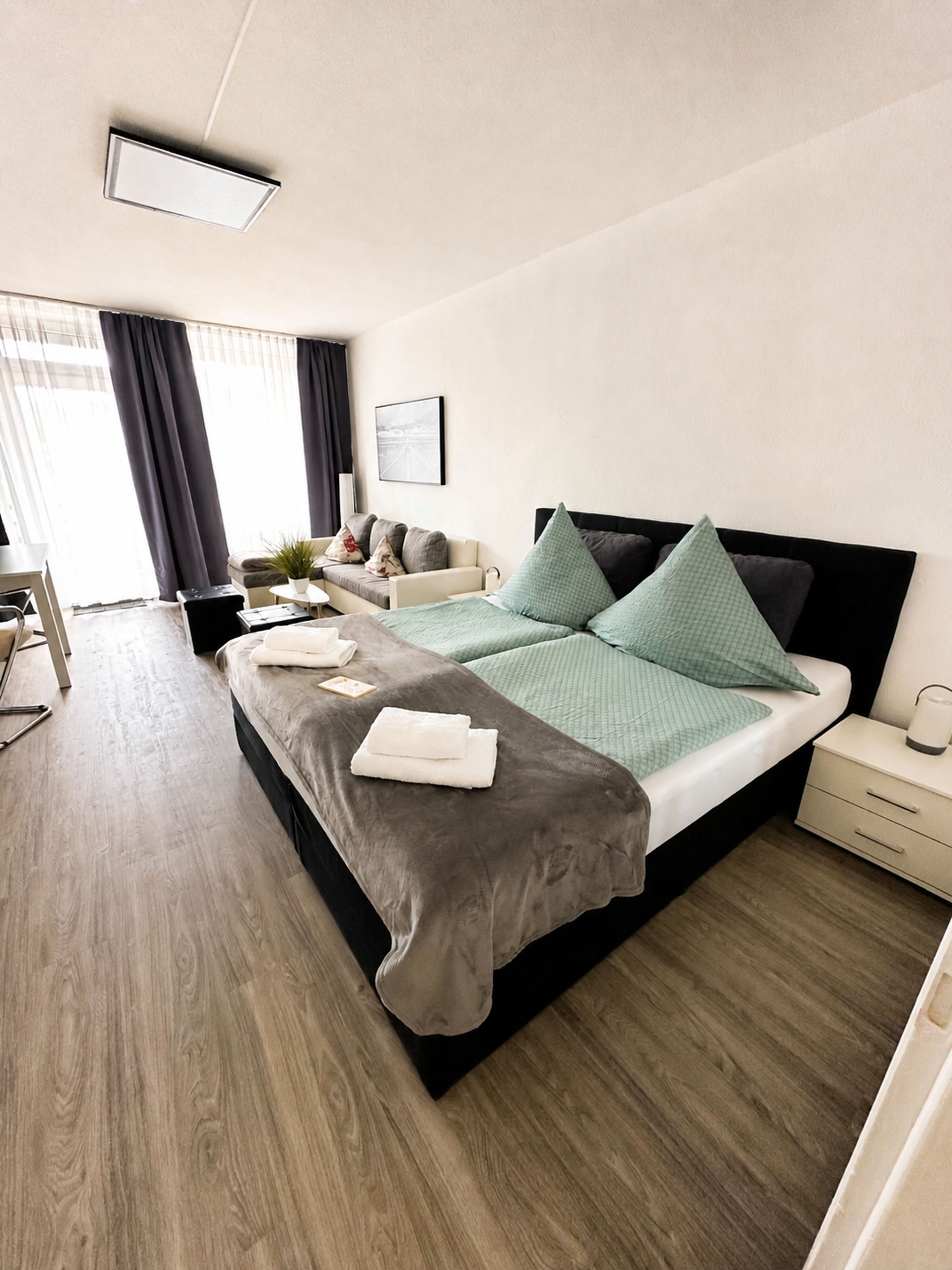 A modern hotel room with a large bed, bedside tables, a desk, and a window with curtains.