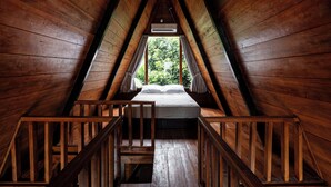 Een houten slaapkamer op zolder met een bed, een raam en een houten trap.
