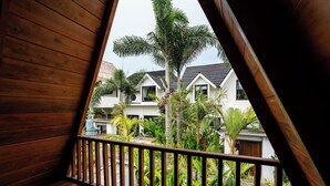 Een houten balkon met uitzicht op een wit gebouw en palmbomen.